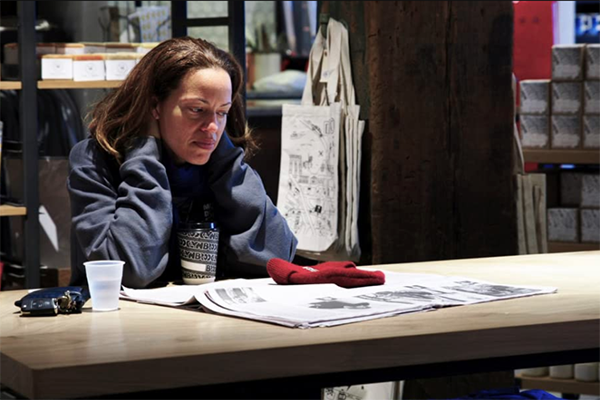 Woman sitting at a table reading a newspaper.